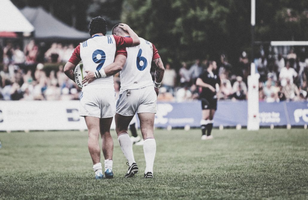 Sports injury insurance. Teammate helps rugby player who had rugby insurance off the pitch with an injury